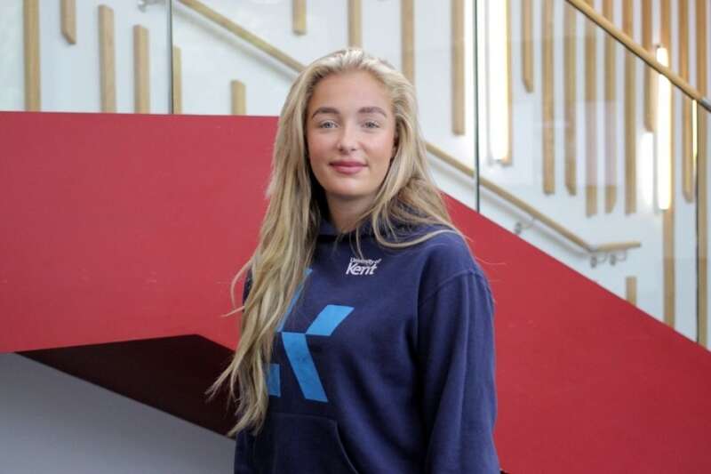 Grace in a blue Kent branded hoodie, posing by the stairs in our Kennedy building.