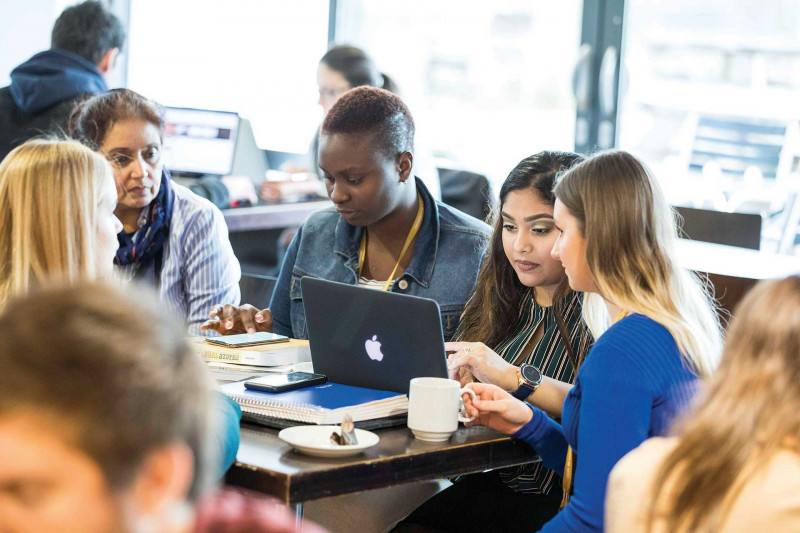 A group of students sit around a table drinking coffee and studying