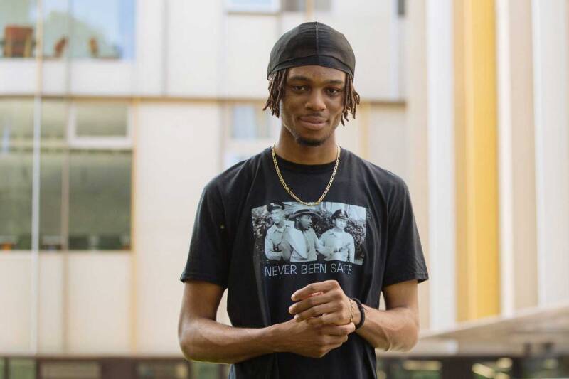 Emmanuel Enemokwu wearing a hat and Never been safe t-shirt, face to camera