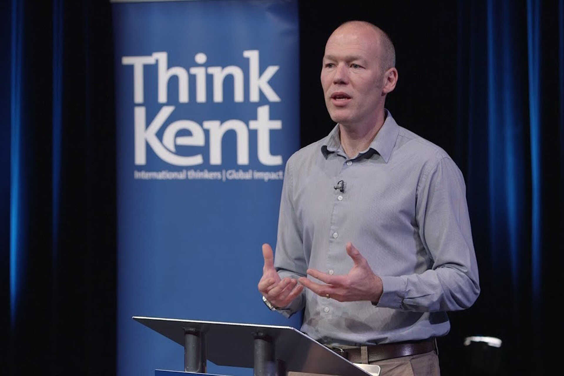 Dr Ben Cocking giving a lecture with Think a Kent banner in the background