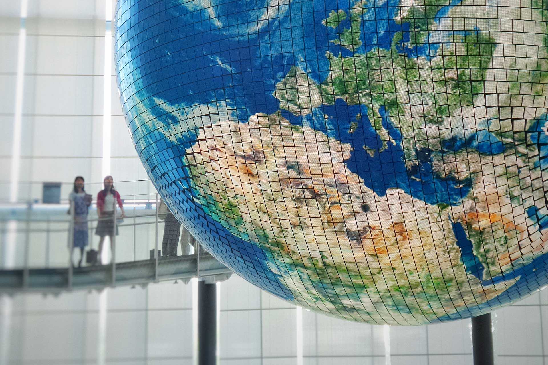 Two people look at a giant mosaic globe