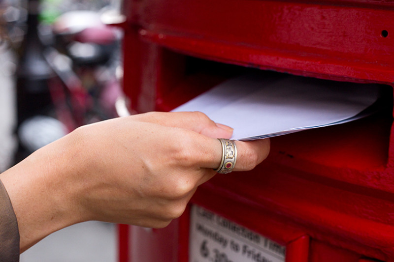 Close up image of someone posting letter into British postbox