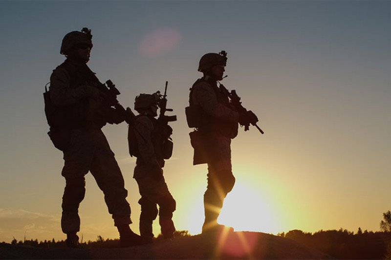 Three soldiers with guns silhouetted against the sky