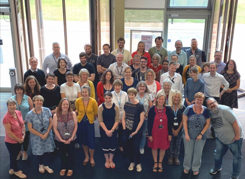 A large group of library staff in the library's welcome hall, smiling up at the camera.