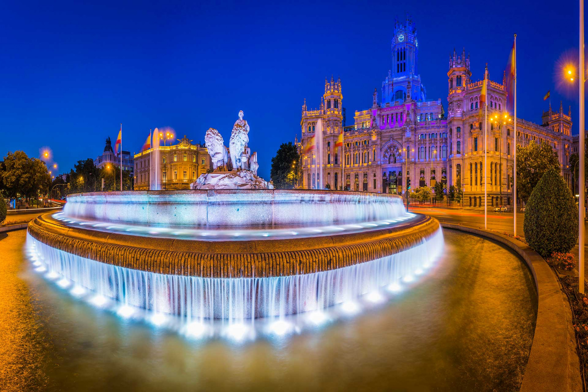 Spotlights illuminate the fountain of Cybele overlooked by the Palacio de Cibeles against the blue dusk skies in Madrid.