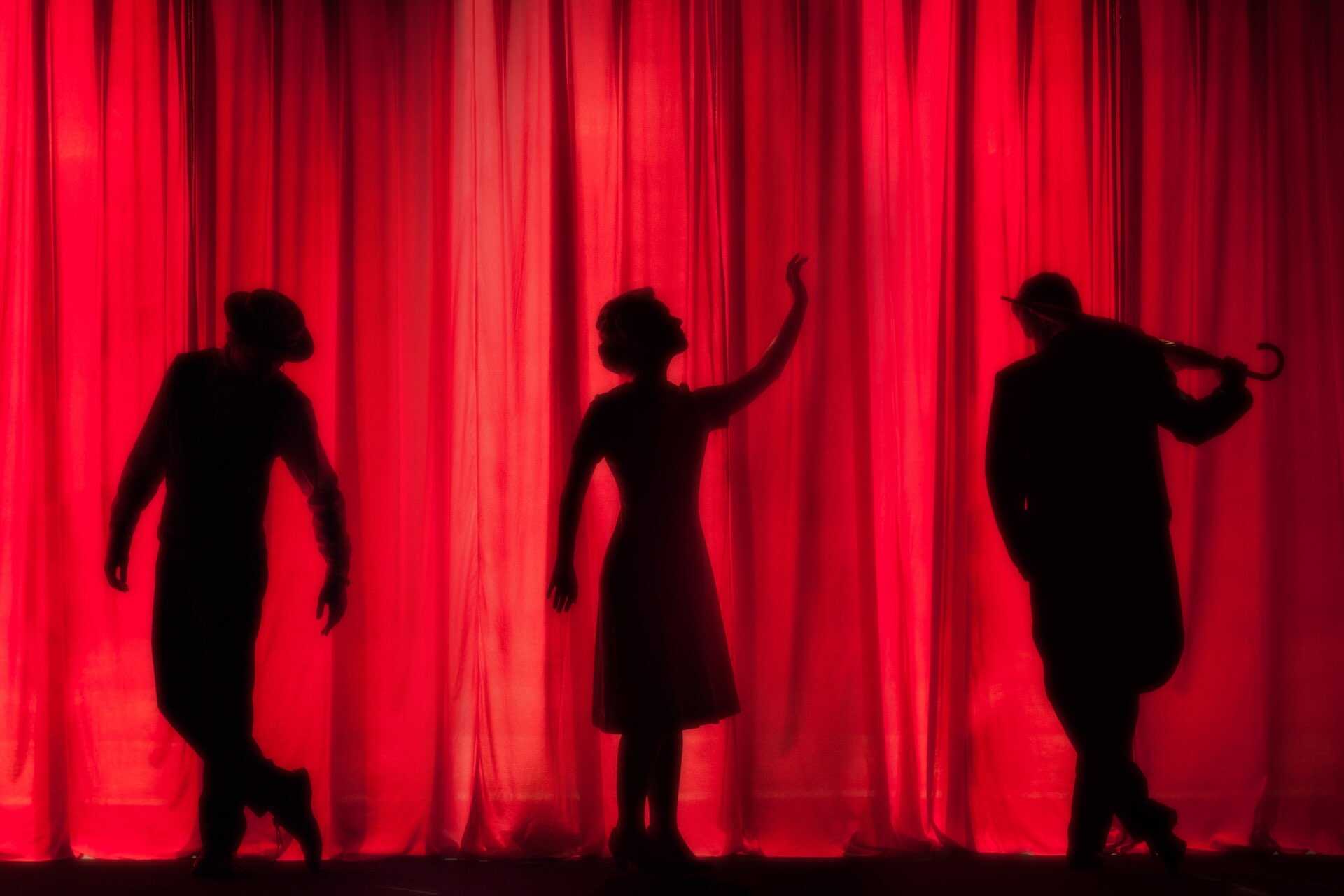 silhouettes of three people against a red curtain