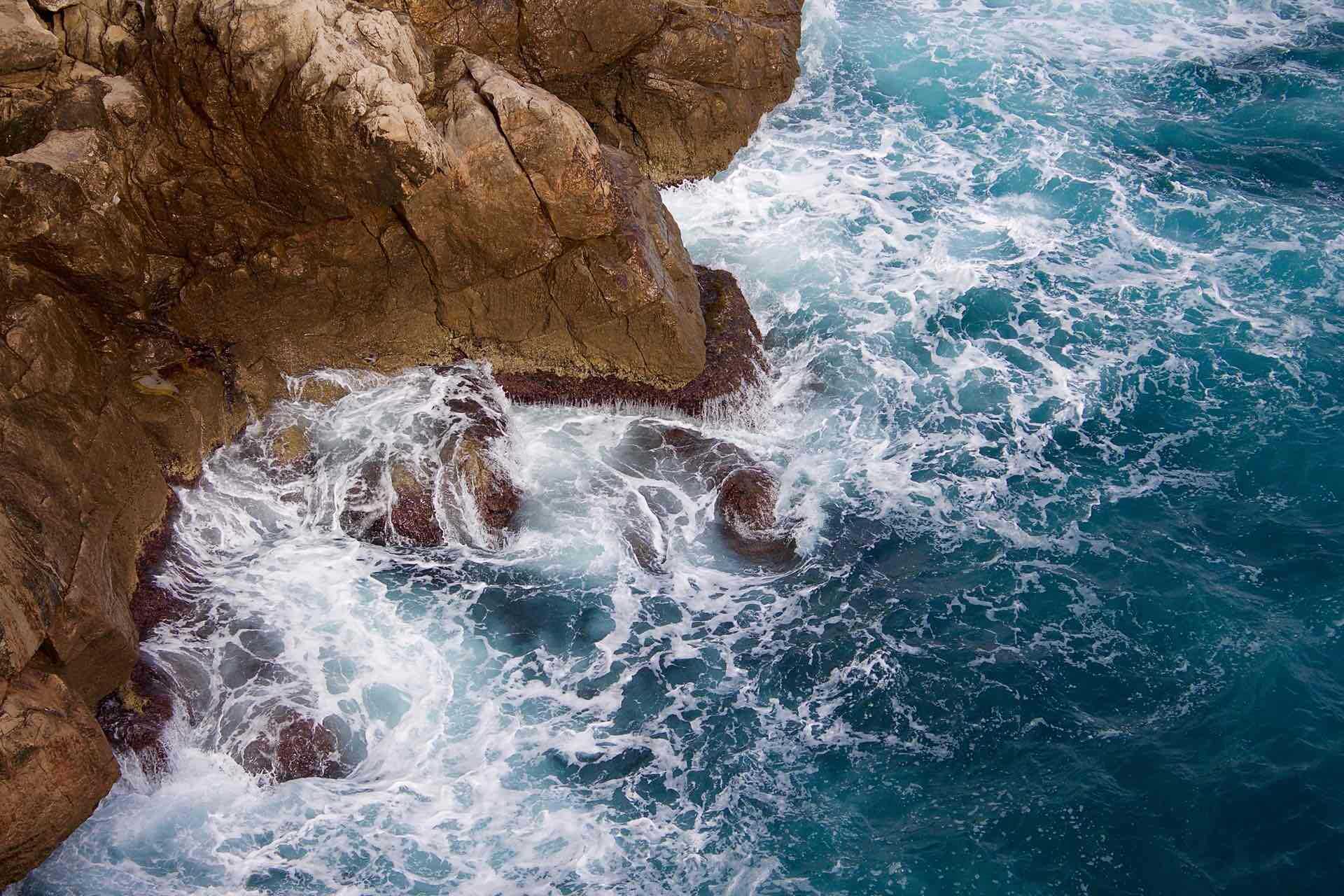 waves crashing against rocks at the foot of a cliff