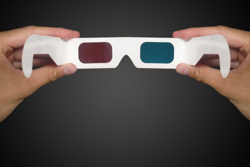 Person holding 3D glasses on a dark background