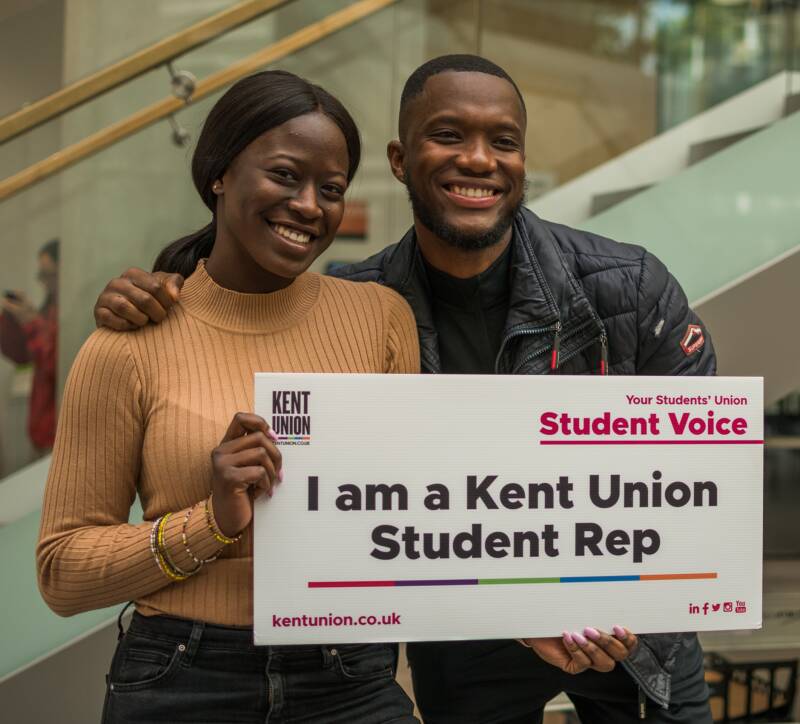 Two students holding board that says "I am a Kent Union Student Rep" and smiling
