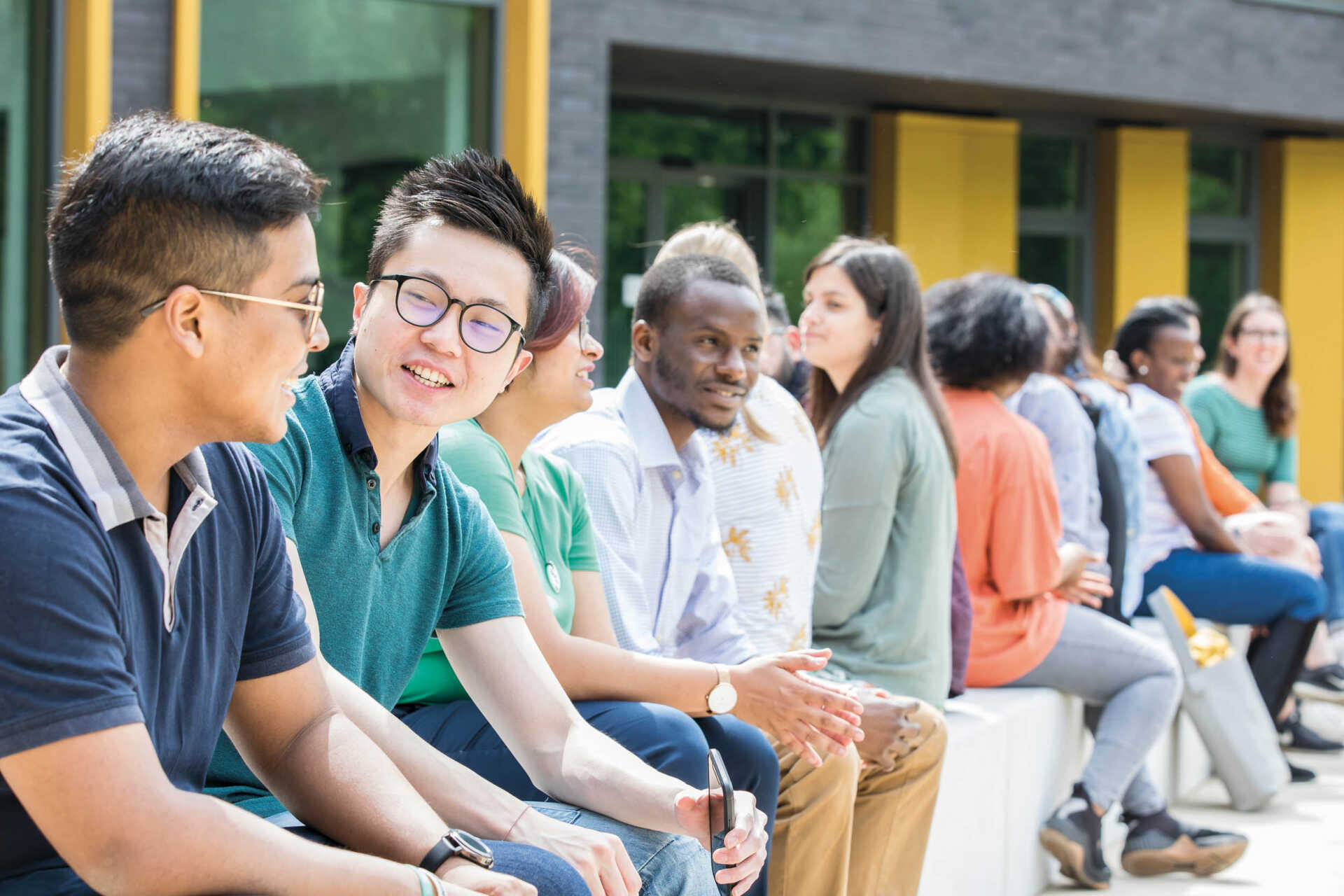 Mix of international and home students sitting on campus bench