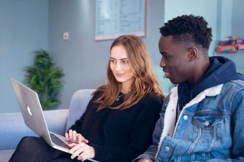 A female and a male student sitting on a sofa and looking at a laptop together