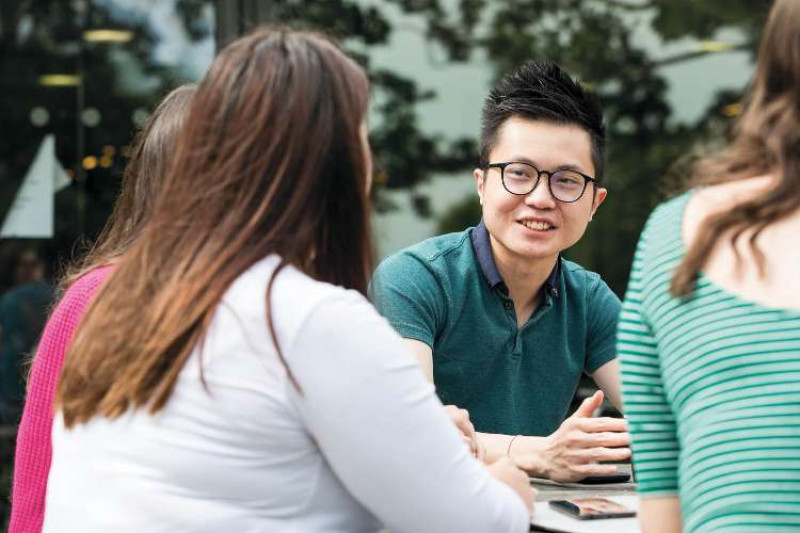 A group of students chatting outdoors, focus on a male student