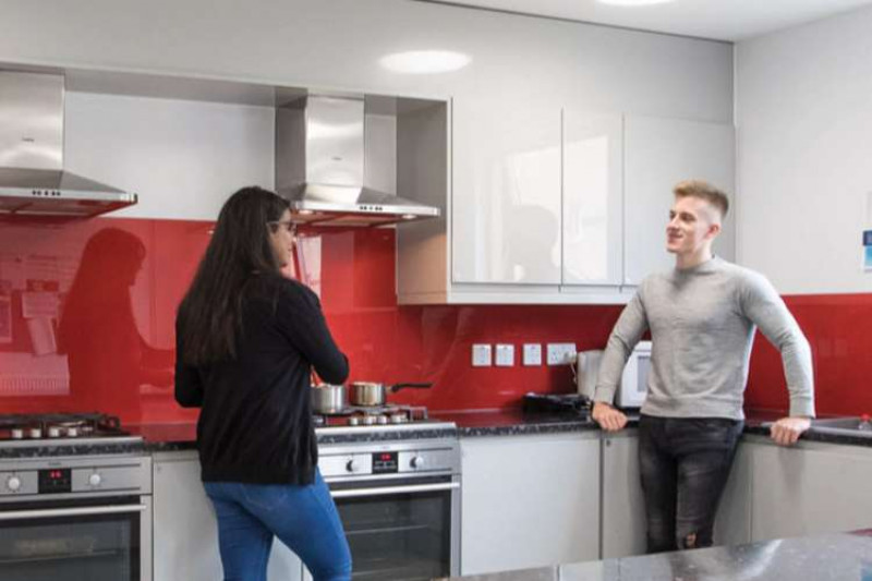 A male and female student chatting in a communal kitchen