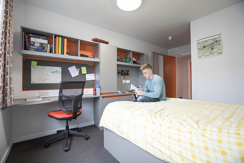 Male student reading a book in Tyler Court B bedroom