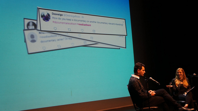 Speakers sit in front of a light blue cinema screen displaying tweets with questions