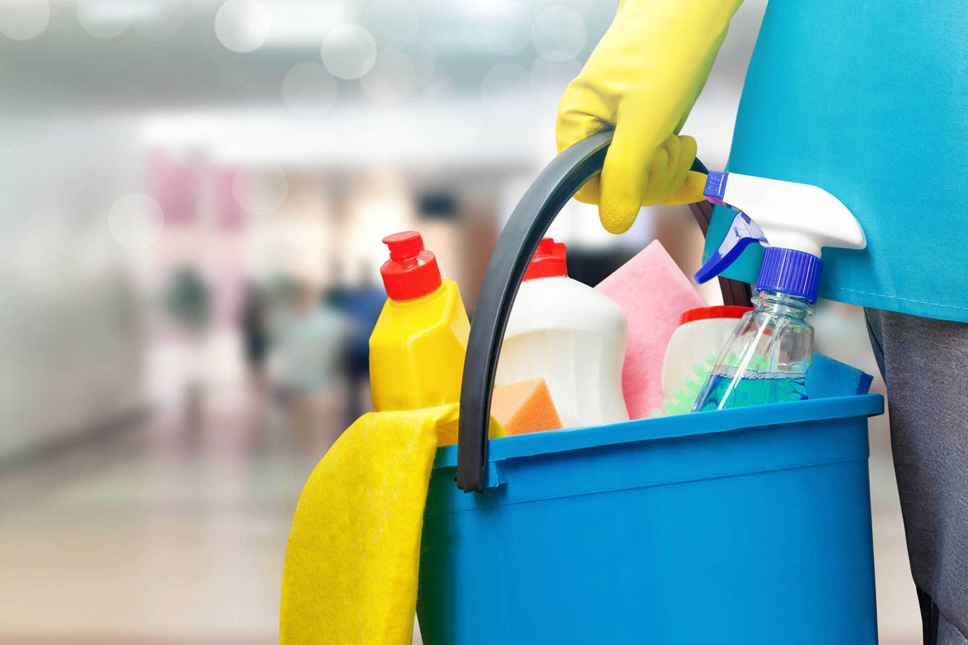 Hand in rubber glove holds bucket of cleaning products