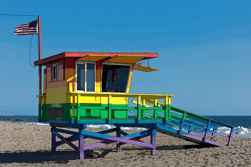 The pride colored lifeguard hut tower in Venice Beach flying the American flag
