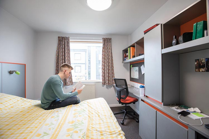 A student reading a book in his campus accommodation bedroom